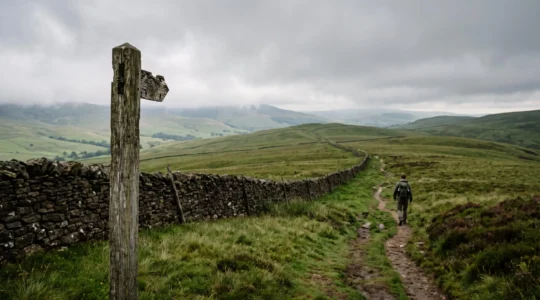 Solo hiker walking a quiet waymarked path across the British countryside with a wooden trail post in the foreground