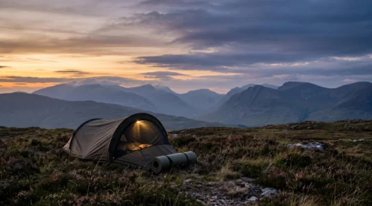 A hiker's hooped bivvy bag pitched on a remote UK hillside at dusk with misty mountains in the background