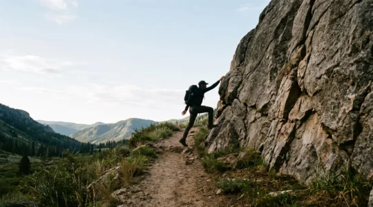 A hiker at the exact point where a dirt trail ends and bare rock requiring hands begins, symbolizing the shift from hiking to scrambling