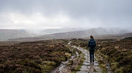 A lone hiker pauses on a misty UK mountain trail, leaving only footprints on the path, embodying Leave No Trace principles