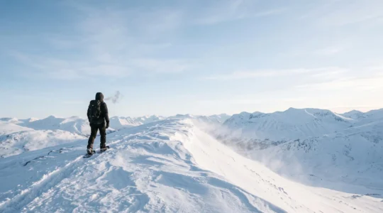 Lone snowshoer crossing a wind-swept frozen ridge under a pale sub-zero dawn sky