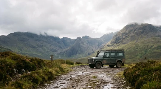 A rugged all-terrain vehicle parked on a rocky, rain-soaked mountain track leading toward misty UK highland peaks