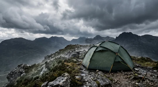 A robust mountaineering tent pitched on an exposed UK mountain ridge holding firm against dramatic storm weather
